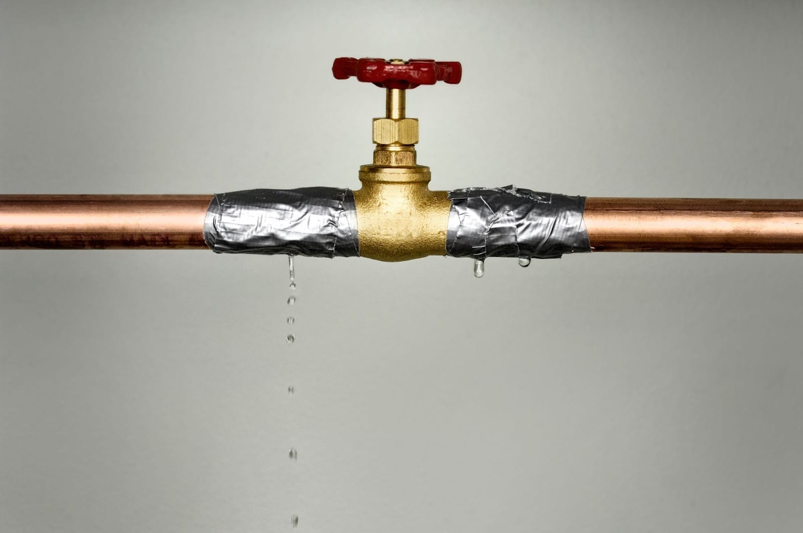 A makeshift repair on a leaking copper pipe with duct tape, failing to stop the drip completely under a closed faucet.