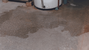 A water heater with signs of leakage, causing a wet patch on a concrete floor.