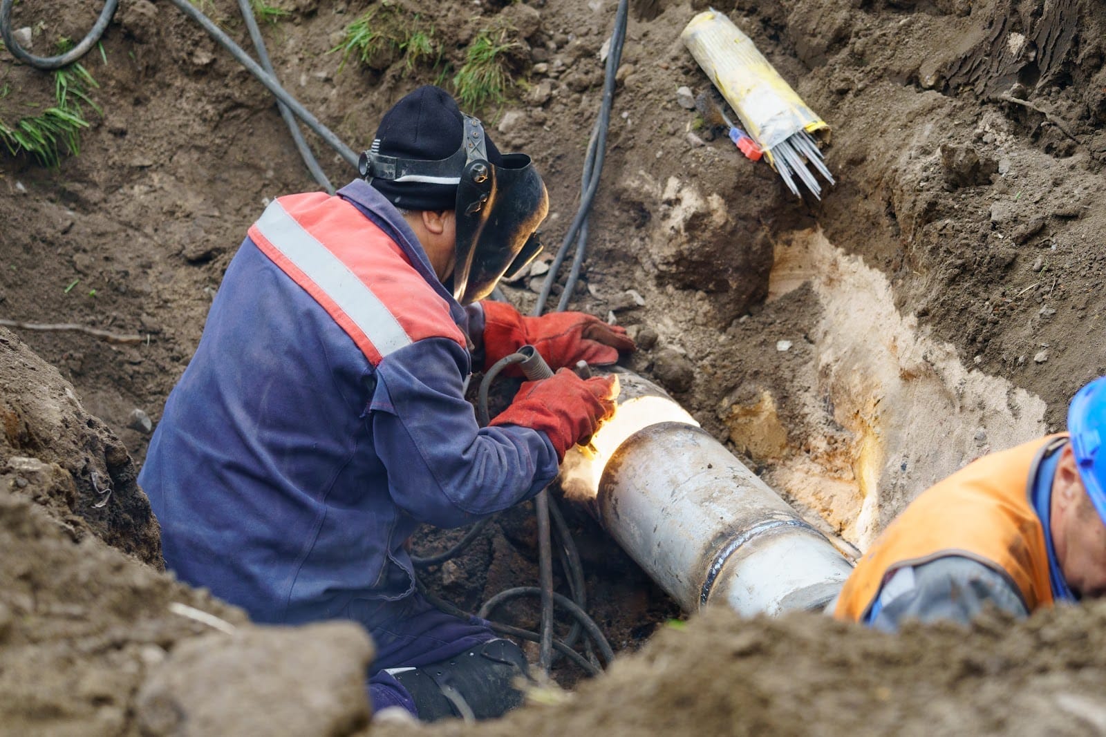 Two men working on a pipe in the dirt.