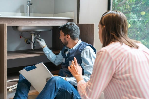 A man and woman looking at a sink in a kitchen.