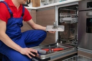 A man fixing a dishwasher in a kitchen.