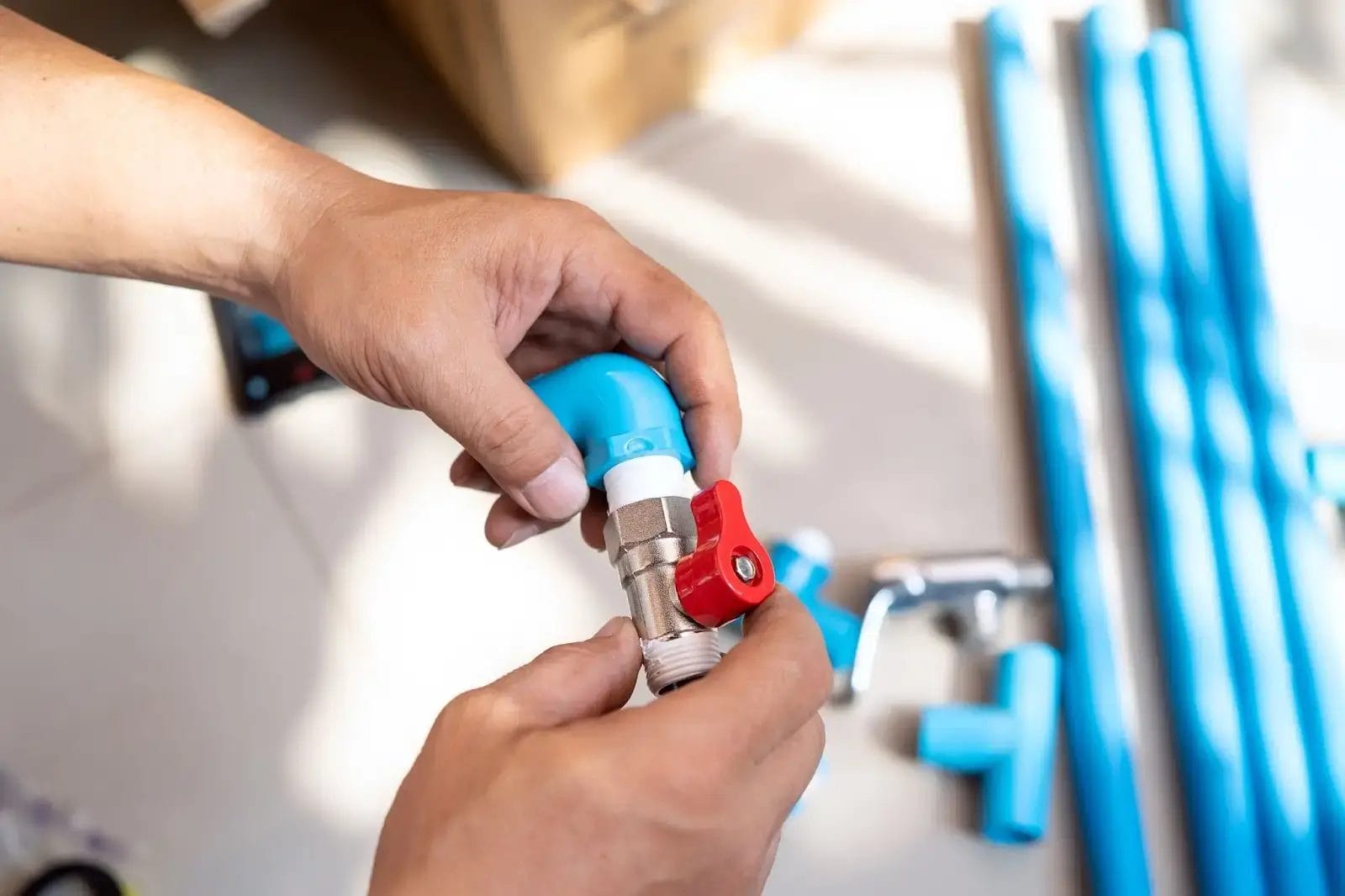 Hands assembling a blue pipe with a red-handled valve, surrounded by blue plumbing parts.