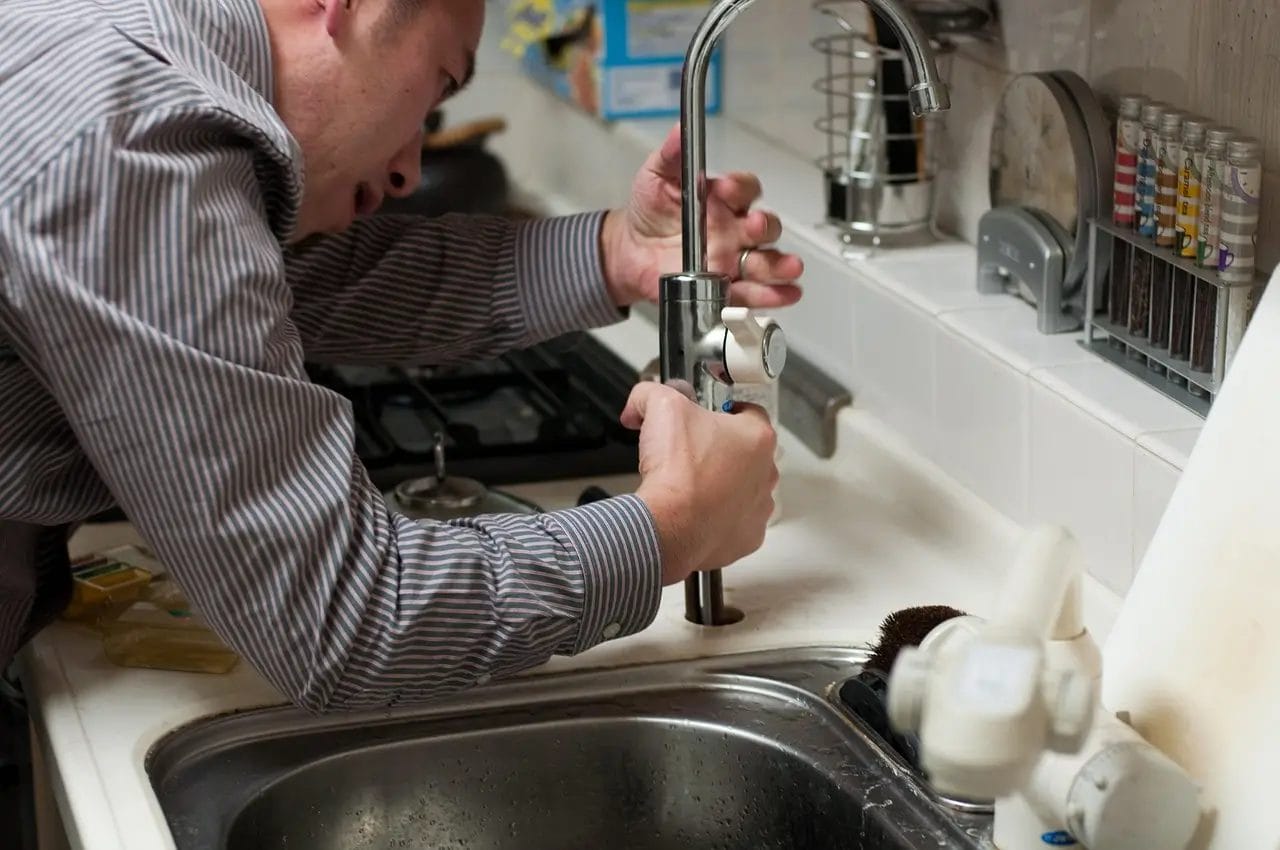 Person in striped shirt fixing a kitchen sink faucet.